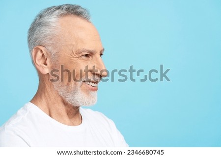 Closeup portrait smiling elderly gray haired man wearing white t shirt isolated on blue background, copy space, face profile. Attractive pensioner posing for picture in studio. Dental care concept