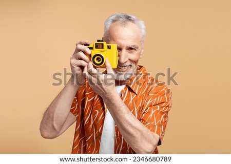 Happy smiling 60 years old man wearing shirt taking photo, using camera isolated on blue background. Attractive elderly male professional photographer, travel concept