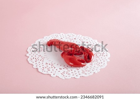 a red metal lobster on a white doily and pink background. Minimal color still life photography 
