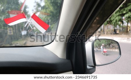Hand holding car steering wheel and  Indonesian flag is affixed to the car windshield to welcome Indonesia's independence day