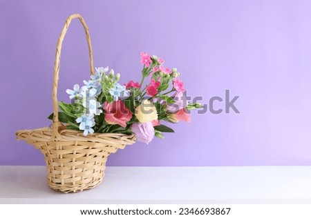 image of delicate pink flowers in the wicker basket over wooden table and purple background