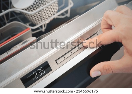 Man pushing start button on the control panel of the dishwasher. Royalty-Free Stock Photo #2346696175