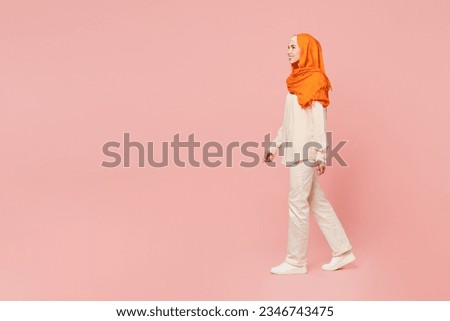 Full body side profile view smiling young arabian asian muslim woman wear orange abaya hijab walk go strolling look aside isolated on plain pink background. Uae middle eastern islam religious concept Royalty-Free Stock Photo #2346743475