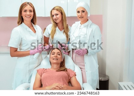 Three beautiful doctors and cosmeticians doing aesthetic procedures on a woman's face Royalty-Free Stock Photo #2346748163