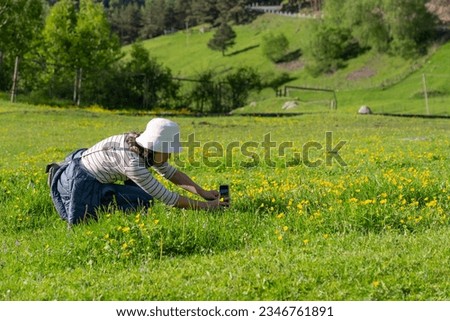 Asian Woman Using Smartphone to Take Photo of Small Flowers in Green Meadow in Countryside of Georgia