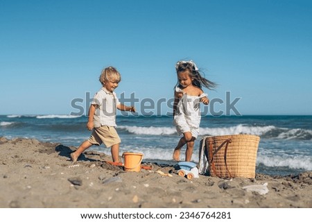 a little blond boy and a little brunette girl run on the beach o