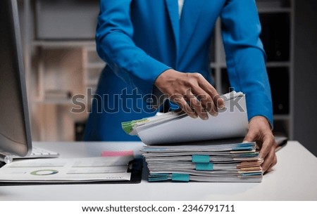 Asian businesswoman searching scattered piles of documents in the office Royalty-Free Stock Photo #2346791711
