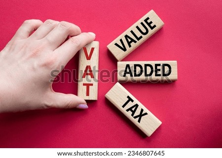 VAT - Value Added Tax symbol. Wooden cubes with word VAT. Businessman hand. Beautiful red background. Business and Value Added Tax concept. Copy space. Concept word