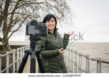 young venezuelan latin woman traveler content creator standing on pier over river in buenos aires, making travel video with her camera for social media, copy space.