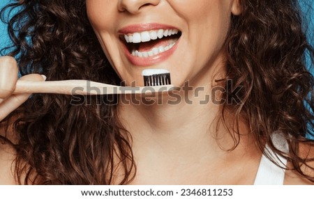Laughing young european curly woman brushing teeth with toothpaste and toothbrush, isolated on blue studio background. Dental care, daily procedures, protection against caries Royalty-Free Stock Photo #2346811253