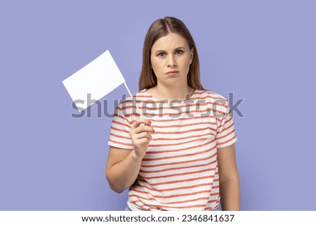 I am give up. Portrait of blond woman wearing striped T-shirt standing and holding white flag and looking at camera with sad face. Indoor studio shot isolated on purple background. Royalty-Free Stock Photo #2346841637