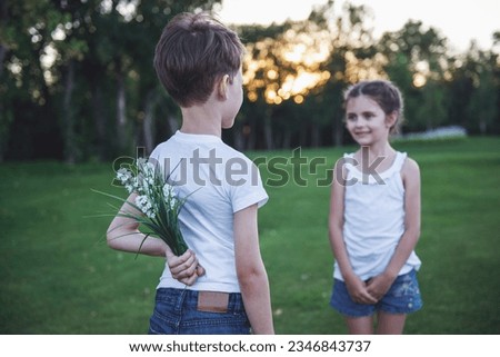 Little boy is holding flowers behind his back for beautiful little girl, she is looking at him and smiling