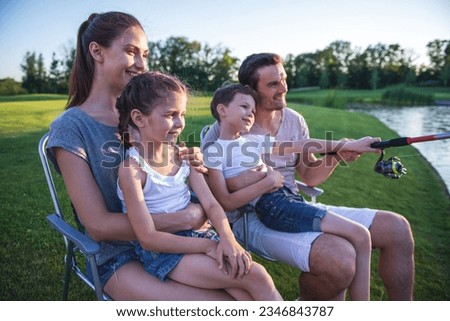 Beautiful happy family is smiling while catching fish in the pond in park. Father and son are holding a fishing rod