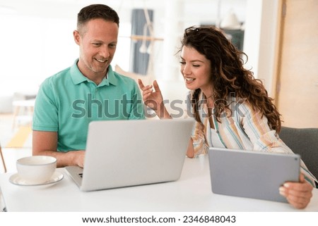 Jovial young couple discussing work using social media and net while drinking coffee in the morning.