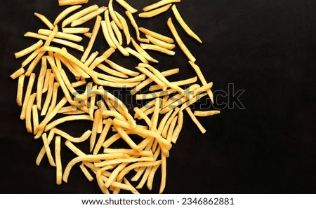 Fried sliced potatoes on a dark background, top view. French fries scattered on a wooden table. Fast food. Cover for the menu Royalty-Free Stock Photo #2346862881