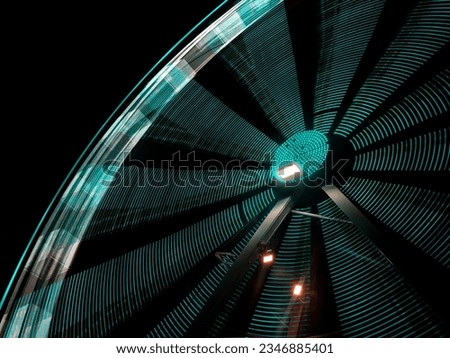 Nocturnal Whirl: A mesmerizing capture of a lit-up Ferris wheel against the night sky, suffused in shades of blue. The deliberate slow shutter speed blurs the lights into captivating streaks, evoking 