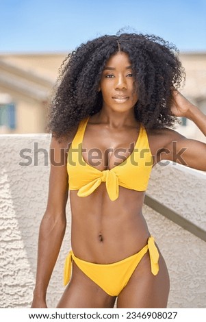 fit and athletic african american woman using medicinal oil for skincare health and beauty wearing yellow bikini