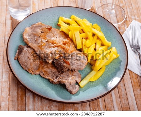 A picture of a pork chop on a plate of fried potatoes.
