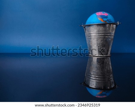 Earth globe in a steel bucket with reflection on a black acrylic board with copy space.