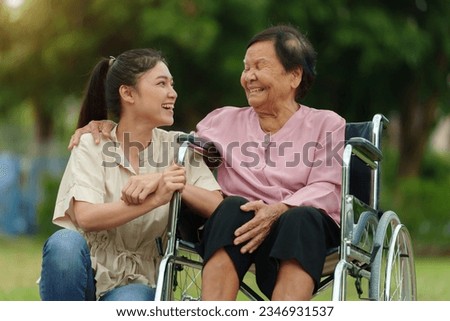 happy young granddaughter talking with senior woman in wheelchair at the park Royalty-Free Stock Photo #2346931537