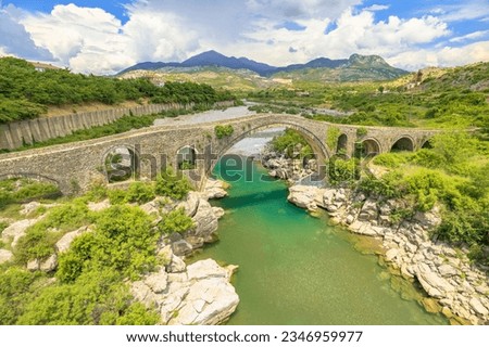 historic Mesi Bridge in Albania. visitors to marvel at its exquisite beauty, immerse themselves in picturesque natural surroundings, and honor rich heritage of this historical landmark. aerial view Royalty-Free Stock Photo #2346959977
