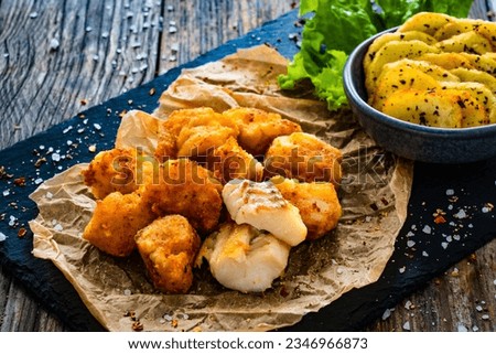 Bakaliaros - seared cod fritters with fried potatoes and fresh vegetables on wooden table 