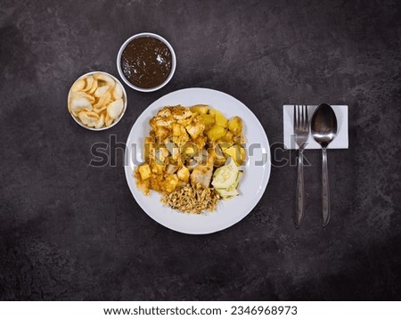 A plate of tahu tek telur with kerupuk or chips and petis sauce on a dark background. Tahu tek is popular dish in Surabaya, an authentic Indonesian food.