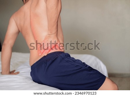 The man sat on the white bed, holding his aching waist as he was about to get up. Inflammation of the lumbar region. Twisting. Getting up in the wrong position. Inflammation of the muscles of the back Royalty-Free Stock Photo #2346970123