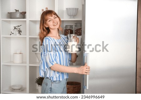 Young woman with jug of milk near fridge in kitchen Royalty-Free Stock Photo #2346996649