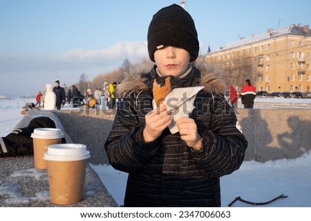 a boy eats a pie and drinks hot tea from cardboard cups on the street on a winter day after riding down a slide. natural light.