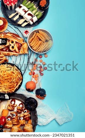 Fun Halloween dinner party table scene on a blue background. Top view. Pizza, pie, spaghetti and snacks.
