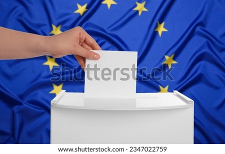 Woman putting her vote into ballot box against flag of Europe, closeup Royalty-Free Stock Photo #2347022759