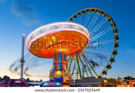 Ferris wheel and other carousels on big german funfair “Cranger Kirmes“ in Herne at blue hour with colorful lights. Long time exposure with multi color light traces (“Kasse“ means cash register)