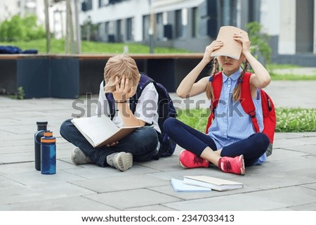Back to school. Schoolchildren are bored reading books and studying homework outdoors. Reusable water bottle. Royalty-Free Stock Photo #2347033413