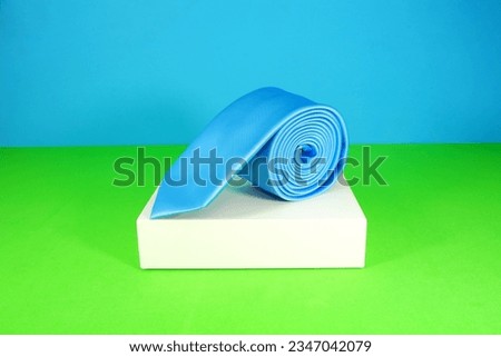 plain blue colour polyester fabric necktie rolled isolated over white gift box with colourful background close up view single object concept nobody 