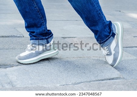 close-up of a woman's feet in jeans and sneakers tripping over unevenly laid paving slabs. Accident, injury on a walk due to poor road surface. Royalty-Free Stock Photo #2347048567