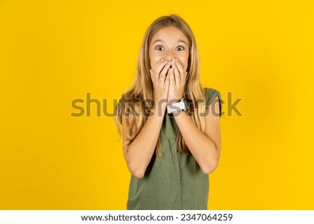 Vivacious beautiful caucasian kid girl wearing green T-shirt , giggles joyfully, covers mouth, has natural laughter, hears positive story or funny anecdote