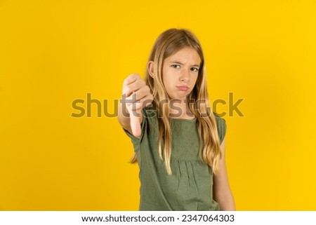 beautiful caucasian kid girl wearing green T-shirt feeling angry, annoyed, disappointed or displeased, showing thumbs down with a serious look