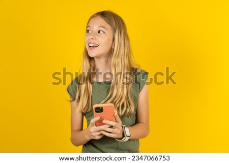 beautiful caucasian kid girl wearing green T-shirt holding a smartphone and looking sideways at blank copyspace. Royalty-Free Stock Photo #2347066753