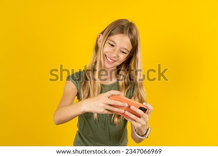 beautiful caucasian kid girl wearing green T-shirt holding in hands cell playing video games or chatting