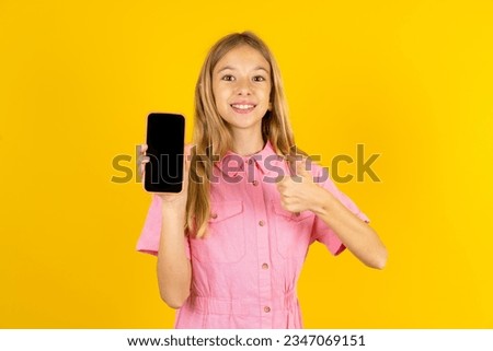 beautiful caucasian kid girl wearing pink dress Show blank screen smartphone, thumb up recommend new app