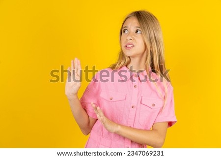 Displeased beautiful caucasian kid girl wearing pink dress keeps hands towards empty space and asks not come closer sees something unpleasant