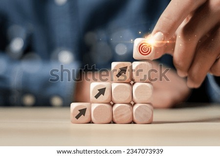 Business management concept. Businessman holding wooden cube stacked with arrow icon pointing to business target. Planning business strategy and setting work goals for success.