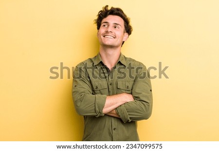 young handsome man feeling happy, proud and hopeful, wondering or thinking, looking up to copy space with crossed arms Royalty-Free Stock Photo #2347099575