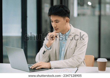 Employee, working with documents sitting at desk using laptop and smartphone at work.