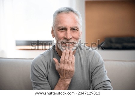 middle aged man sitting on sofa looking at camera smiling and communicate with sign language by video call. senior male learning hand gesture for deaf, webcam view