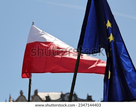 Flags of Poland and EU wave together on flag poles against blue sky