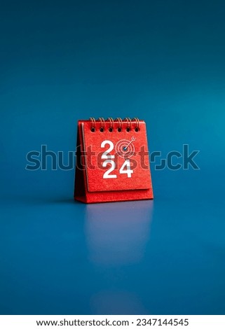 Happy new year 2024 vertical background. 2024 numbers year with target dart icon on red small desk calendar cover standing on blue background, minimal style. Business goals plan and success concepts.