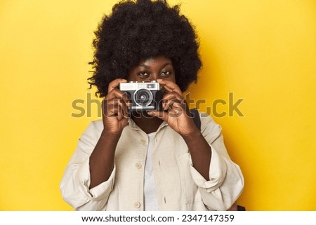 African-American woman with a vintage camera on a yellow studio background.