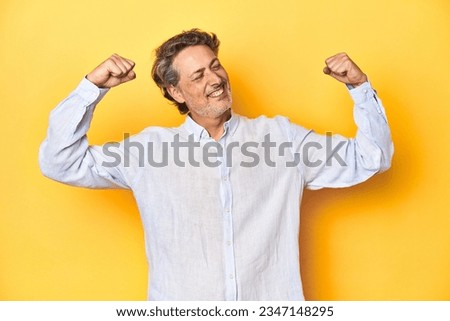 Middle-aged man posing on a yellow backdrop raising fist after a victory, winner concept. Royalty-Free Stock Photo #2347148295